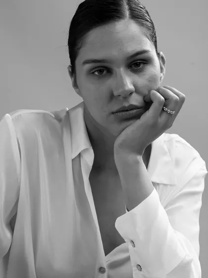 A raw and honest black and white portrait. The model's contemplative pose, with her hand resting on her chin, naturally brings the elegant ring into focus. The minimal styling ensures the jewellery remains the hero.