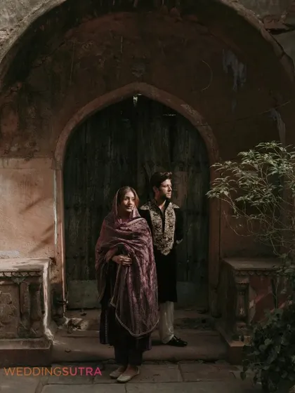 A moody and atmospheric portrait of the couple framed by an old archway. The lighting and composition create a cinematic and timeless feel.
