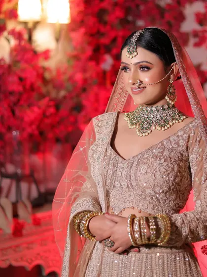 A candid, happy shot of the bride in her pastel lehenga. Her natural smile and the soft lighting create a warm and inviting portrait against the vibrant red background.