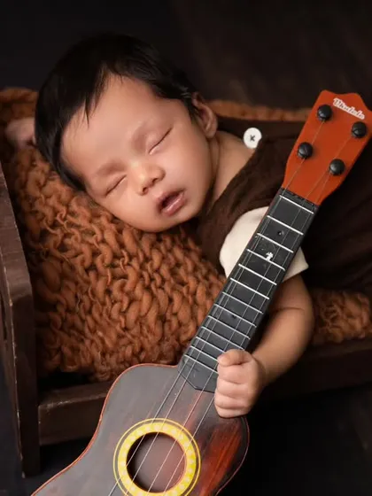 A little musician in his dreams. This newborn portrait features a tiny ukulele, creating a sweet and peaceful image of a sleeping baby.