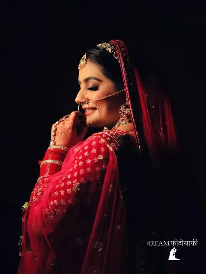 A classic low-light portrait of bride Nikita in her red lehenga, her smile and nath shining through the shadows.