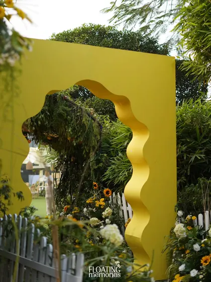 A bright yellow, wavy archway served as a picturesque entrance to one of the garden areas. This modern and playful architectural element was a beautiful frame for the floral arrangements within.