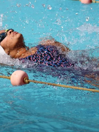A swimmer demonstrates powerful backstroke form, splashing through the lane.