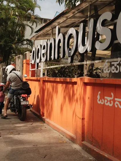 Happy 1st Birthday, Openhouse Indiranagar! A shot of our iconic orange wall and a father arriving with his child on a motorcycle celebrates our first year and the 800+ families who have joined us.