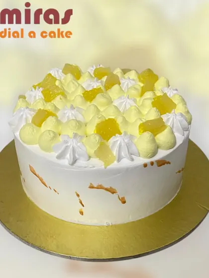 A bright and sunny pineapple cake. The white frosting is topped with swirls of yellow cream and chunks of pineapple, offering a refreshing and tropical flavor.
