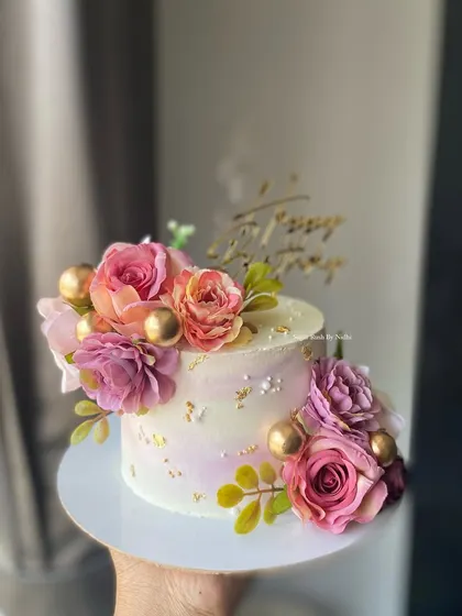 A beautiful floral cake with a pink ombre effect. This design is decorated with an abundance of fresh flowers and gold spheres for a lush and celebratory look.