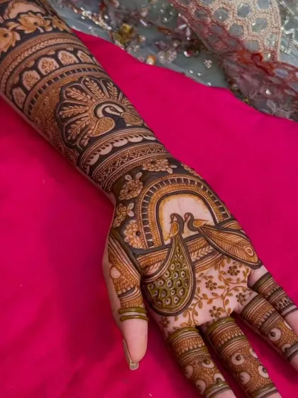 A full-hand and arm design dominated by graceful peacock figures. The details in the feathers and the surrounding patterns are meticulously done.