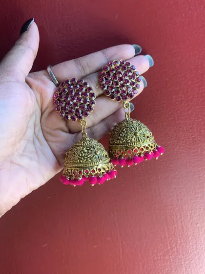 A hand-held view of the grand pink stone-studded jhumkas, showing their size and sparkle.