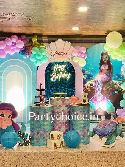 The main stage for our mermaid theme, featuring character cutouts of Ariel, an under-the-sea backdrop, and balloon arches in shades of blue, purple, and green to mimic ocean waves.