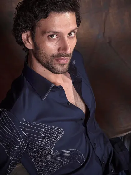 A closer, more intense portrait featuring the bird embroidered shirt. It's a piece that combines artistry with everyday wearability.