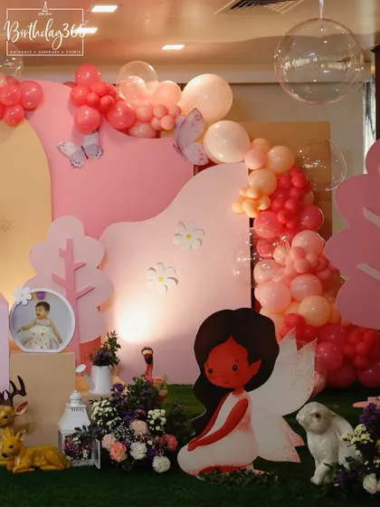 A whimsical scene from a fairy party, featuring a large angel-wing cutout, friendly animal props, and a soft pink color palette.