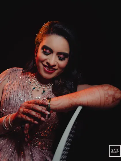 A lovely portrait of the bride admiring her henna-adorned hands, seated and smiling during her evening celebration.