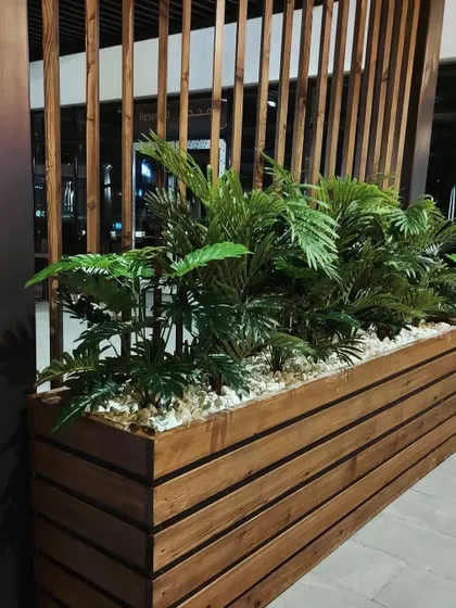 A simple yet effective way to divide a space and add greenery. This long wooden planter filled with artificial palms adds a natural touch to a commercial walkway while maintaining an open feel.