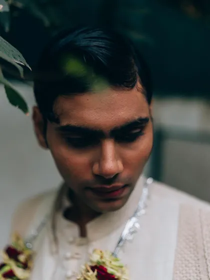 A close-up portrait for Sanchit Sharma, framed by leaves. The soft, natural light and downward gaze create a gentle and introspective mood.