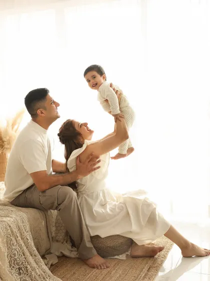 A classic family portrait with a playful twist. The mother lifting her child high in the air brings a sense of motion and pure happiness to this cozy, boho-themed shot.