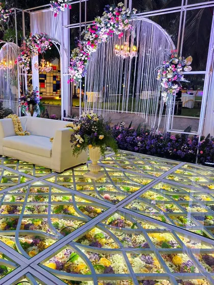 A stunning view of the illuminated floral floor and stage. The combination of the glass floor, intricate arches, and hanging chandeliers creates a truly magical and luxurious setting for a reception.