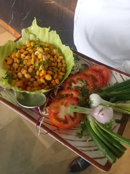A simple yet flavorful corn chaat served in a lettuce cup. This dish is a light and healthy starter, presented beautifully on a platter with fresh tomato and spring onion garnish.