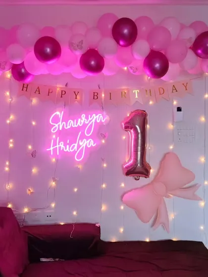 A sweet and simple first birthday decoration for a small space, using a neon sign, fairy light curtain, and a pink balloon garland.