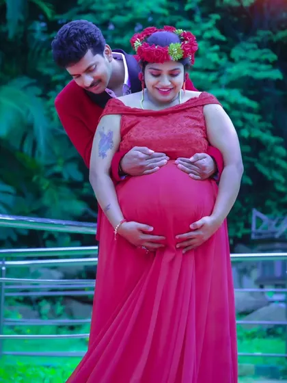 A tender moment between the expecting couple, framed by the lush greenery of an outdoor location.