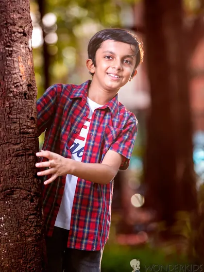 A boy peeks out from behind a tree with a playful smile. The natural setting and his spontaneous expression make this a charming and candid outdoor portrait.