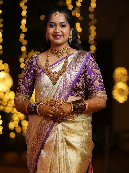 Our client radiates timeless elegance in a deep purple silk blouse with intricate gold zari embroidery. The traditional floral and vine motifs are meticulously crafted, adding a luxurious, regal charm to her Kanjeevaram saree.
