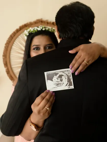 A creative announcement shot. The mother-to-be peeks over her partner's shoulder while holding the sonogram, creating a sense of mystery and excitement.