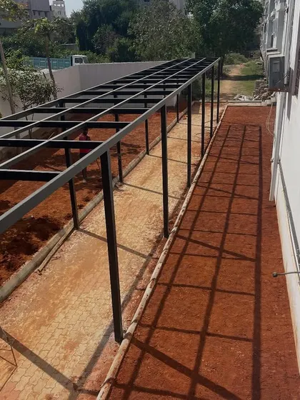 The same walkway during the construction phase, showing the metal pergola frame and the prepared red soil base before the lawn was laid.