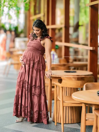 A candid shot of a mother-to-be in a lovely rust-colored boho dress, taken in a cafe-like setting, showcasing versatile indoor location options.