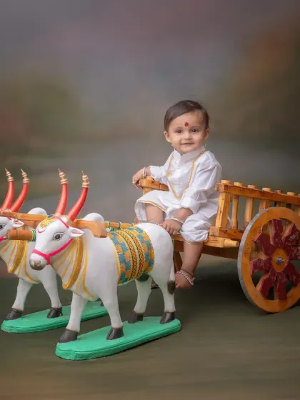 A simple and classic portrait featuring a baby in a white kurta sitting on a decorative bullock cart. This Bail Pola inspired theme is a wonderful way to connect with Maharashtrian agricultural traditions.