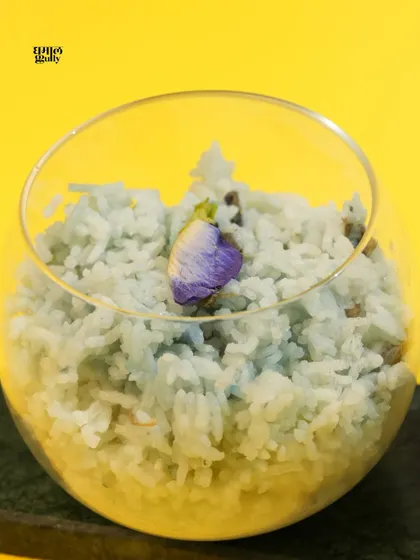 A focused shot of my blue jasmine rice, naturally colored with butterfly pea flowers. The single edible flower on top emphasizes the delicate, artistic nature of my cooking. It's the perfect, beautiful accompaniment to my Thai curry.