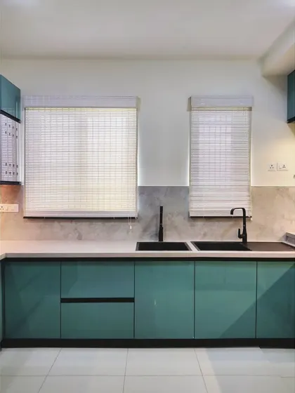The sink area of the teal kitchen, featuring a modern black faucet and double sink. The roller blinds provide privacy while allowing natural light to illuminate the space.