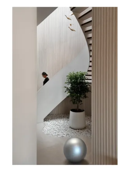 A view of the helical staircase from the side, showing how it carves a path through the space, complemented by a small indoor garden of white pebbles and greenery.