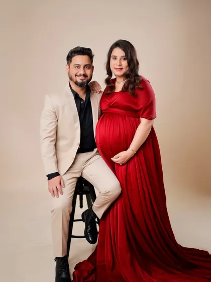 A beautifully composed portrait of an expecting couple. The man is seated while his partner stands, creating a dynamic and connected pose.