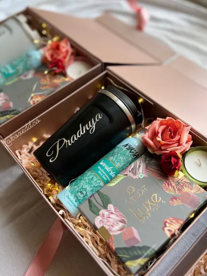 An inside look at one of our custom bridesmaid hampers. This one features a personalized tumbler, a scented candle, luxury chocolates, and a face mask, all nestled in a keepsake box with floral accents.