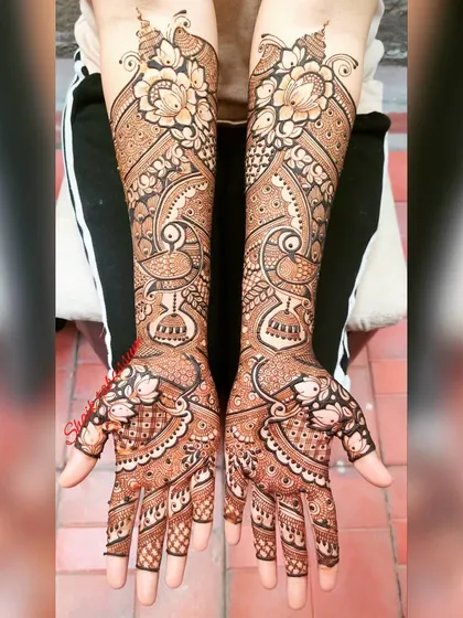 This elegant design features bold floral patterns at the top, flowing into graceful peacock motifs and intricate jaali (net) work covering the hands and arms.