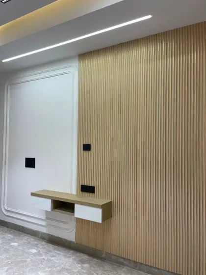 This cozy wall design is perfect for a TV unit. It features a combination of white molded paneling and light wood fluting, with a floating shelf that is both stylish and practical.