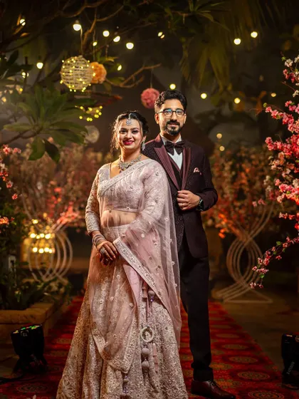 A classic reception portrait. The couple stands together against a backdrop of beautiful floral decorations and warm lights, looking elegant and happy.