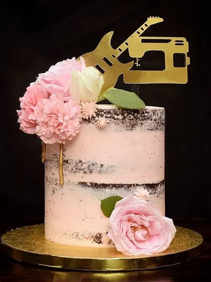 A rustic semi-naked wedding cake for a couple's special day. This design combines exposed chocolate cake layers with light pink buttercream, fresh flowers, and a custom topper reflecting the couple's hobbies of music and sewing.