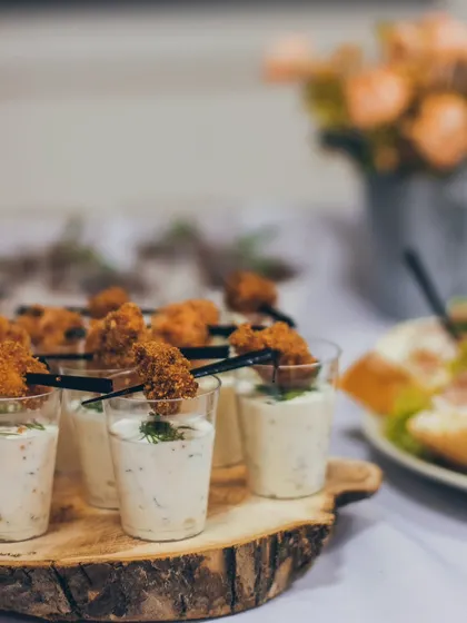 Bite-sized appetizers in clear cups, featuring a creamy dip topped with a crispy element.