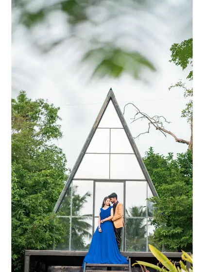 A modern fairytale scene in front of a stylish A-frame cabin. The bride's royal blue gown stands out beautifully against the lush green forest backdrop.