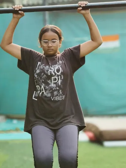 This strong girl is working on her pull-up strength. Her determination is clear in her focused expression.