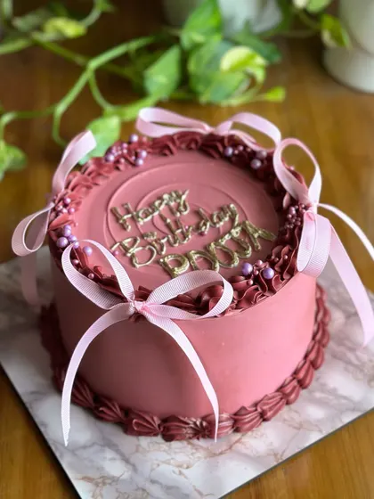 A slice of Victorian charm with a modern, minimal touch. This cake features a rich mauve color, delicate piping, and pretty pink ribbons for a simple yet elegant birthday.