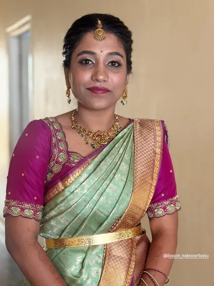 This client is ready for her muhurtham ceremony. The mint green and magenta saree is draped in a classic style, complemented by a traditional gold vaddanam (waist belt) that holds the pleats in place.
