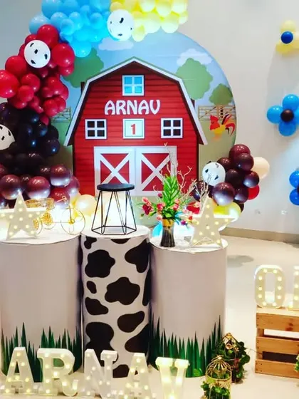 I designed this farmyard theme for a first birthday party. The centerpiece is a red barn backdrop with the child's name, surrounded by balloon arrangements and pedestals with cow-print details to match the farm animal theme.