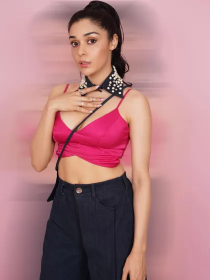 Actress Eisha Singh in a vibrant, high-fashion studio setup. The pink bralette and unique pearl-studded accessory create a trendy and youthful look.