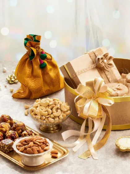 This cozy festive hamper includes a tray of assorted nut laddoos, bowls of cashews and almonds, and a decorative potli, all arranged in a charming round gift box.