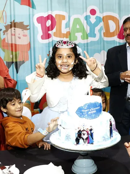 The birthday girl, complete with a tiara and a smile, poses with her Frozen-themed cake. The joy on her face is why I love my job.