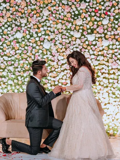 A picture-perfect proposal moment during an engagement ceremony, set against a stunning wall of pastel-hued flowers.