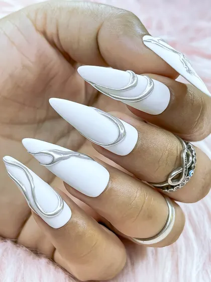 A stunning matte white stiletto nail set with abstract, free-flowing 3D silver chrome details. A perfect example of modern, minimalist-yet-bold design.