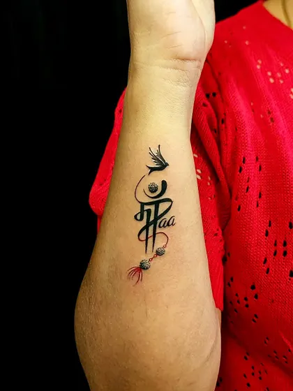 This custom calligraphy piece combines 'Maa' and 'Paa' (Mother and Father) into a single, flowing design. It’s a tribute to the foundation of family, adorned with a feather and beads.